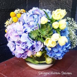 Bouquet of blue and lavender hydrangeas with yellow tulips in a bowl vase
