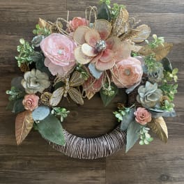 Decorative floral wreath with pink and gold flowers on a wrapped ring base
