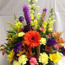 Mixed bouquet in a wicker basket with orange, purple, yellow, and pink flowers