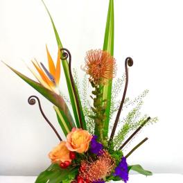 Tall tropical flower arrangement in a patterned vase with orange and purple blooms