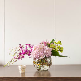 Pink and green orchid arrangement in a round glass vase with a small candle nearby