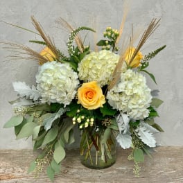 Yellow roses and white hydrangeas in a glass vase with dried grasses