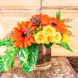 Orange gerbera daisies and yellow roses in a glass vase