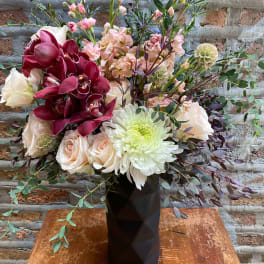 Mixed bouquet in a black vase with burgundy orchids and pale roses