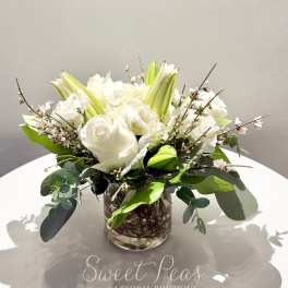 White roses and lilies arranged in a clear glass vase with greenery