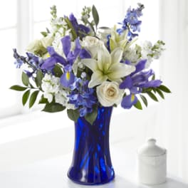 Blue and white bouquet with lilies, roses, irises, and delphinium in a cobalt glass vase