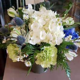 White and green floral arrangement with blue thistle in a vase