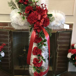 Tall red carnation funeral spray with white ruffles and a red ribbon on an easel