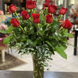Red roses arranged in a clear glass vase with mixed greenery