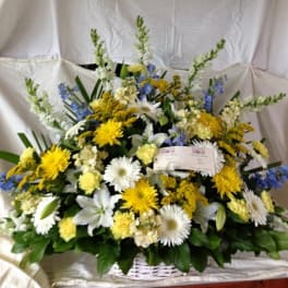 Large mixed floral arrangement in a white basket with yellow, white, and blue blooms