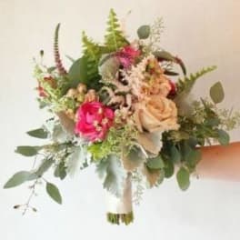 Handheld bouquet of pink and peach roses with greenery