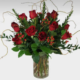 Red roses arranged in a clear glass vase with greenery and berry accents