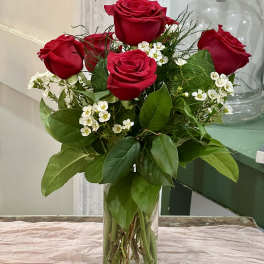 Red roses arranged in a clear glass vase with white filler flowers