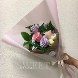 Pastel bouquet of pink and lavender roses wrapped in pink paper with a satin ribbon bow