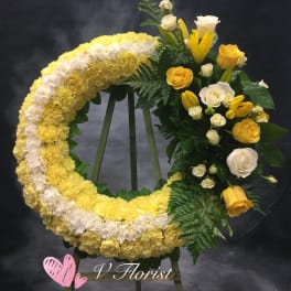 Crescent standing wreath of yellow and white carnations with yellow lilies and roses on a wooden easel.