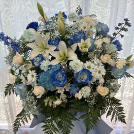 Tall blue and white standing flower arrangement with lilies, roses, and daisies on a tripod stand