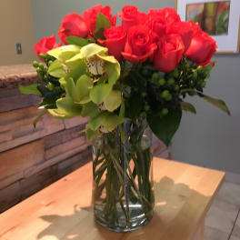 Red roses and green orchids arranged in a clear glass vase