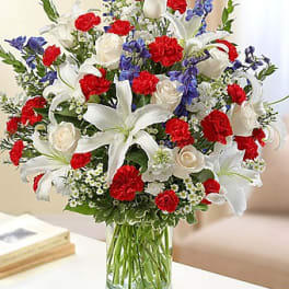 Bouquet of white lilies, red carnations, blue flowers, and white roses in a glass vase