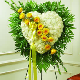 Heart-shaped white floral wreath with yellow roses on a stand