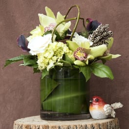 White and pale green floral arrangement in a glass vase with a small bird figurine
