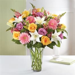 Mixed bouquet of roses, lilies, and pink daisies in a clear glass vase