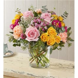 Mixed bouquet of pink, yellow, and peach roses in a clear glass vase