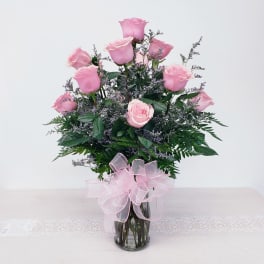 Pink roses arranged in a clear glass vase with a pink ribbon bow