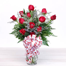 Red roses in a clear glass vase with a heart-patterned bow
