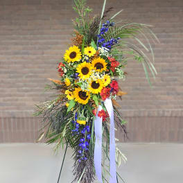 Tall standing floral spray with sunflowers, blue flowers, and ribbon streamers