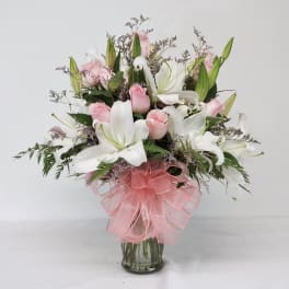 Pink roses and white lilies in a glass vase with a pink bow