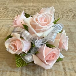 Small cluster of pale pink roses accented with silver and white ribbon on a wood surface