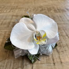 White orchid corsage with silver ribbon and bead accents on a wooden surface