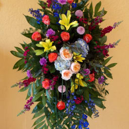 Tall standing floral spray with roses, lilies, and blue blossoms