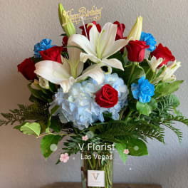 Bouquet of red roses, white lilies, and blue hydrangea in a glass vase