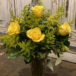Yellow roses arranged in a clear glass vase with airy green filler