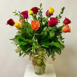 Mixed roses in red, pink, yellow, and orange arranged in a glass vase