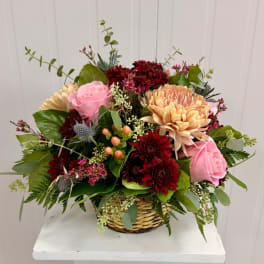 Basket arrangement of pink roses, burgundy mums, and peach blooms