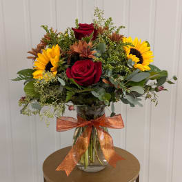 Bouquet of red roses and sunflowers in a glass vase with an orange ribbon