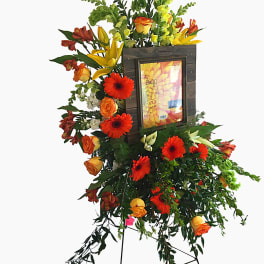 Tall floral easel arrangement with orange and yellow blooms around a framed photo