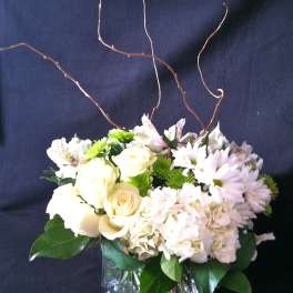 White floral arrangement in a square glass vase with curly branches