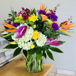 Colorful tropical bouquet in a clear glass vase with orchids and roses