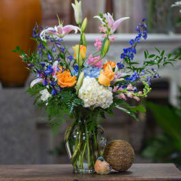Mixed bouquet in a glass vase with orange roses, lilies, hydrangea, and blue flowers
