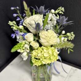 White and pale green bouquet with blue accents in a glass vase