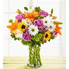 Mixed bouquet of roses, lilies, daisies, and sunflowers in a glass vase