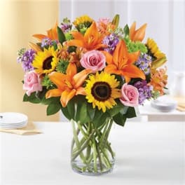 Bouquet of sunflowers, orange lilies, and pink roses in a glass vase