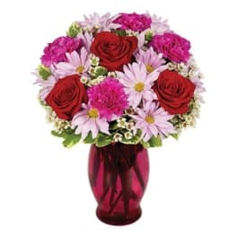 Bouquet of red roses and pink daisies in a red glass vase
