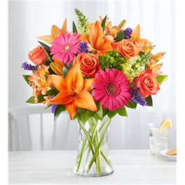 Mixed bouquet of orange lilies, pink gerbera daisies, and roses in a glass vase