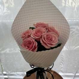 Small bouquet of pink roses wrapped in textured white paper with a black ribbon.