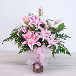 Pink lilies and roses in a vase with a pink ribbon bow