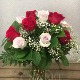 Arrangement of red and pale pink roses with white filler flowers in a clear glass vase on a wooden surface